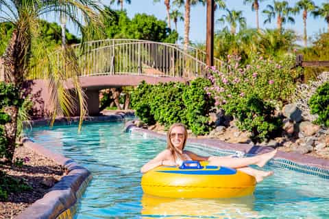Woman on yellow float in tropical lazy river with arched bridge and flowering vines