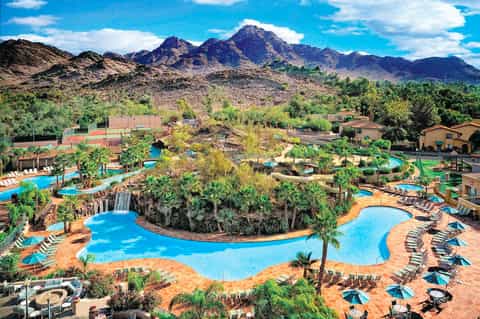 Expansive resort pool complex with multiple pools surrounded by palm trees and desert mountains in background