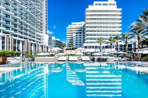 Resort pool with crystalline blue water reflecting modern white buildings and palm trees under blue sky