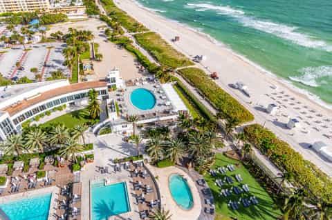Aerial view of beachfront resort with circular pool, multiple loungers, and sandy beach
