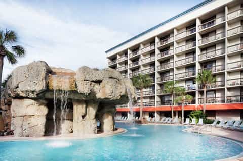 Resort pool with distinctive rock waterfall feature, multi-story building, and lounge chairs