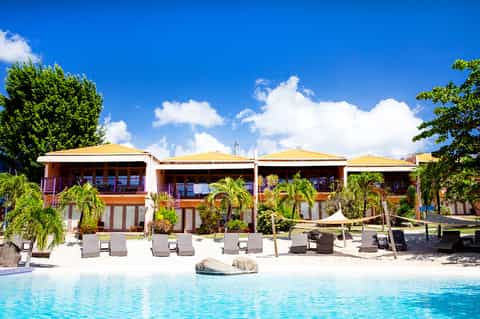 Beachfront resort building with yellow roofs, palm trees, and turquoise pool