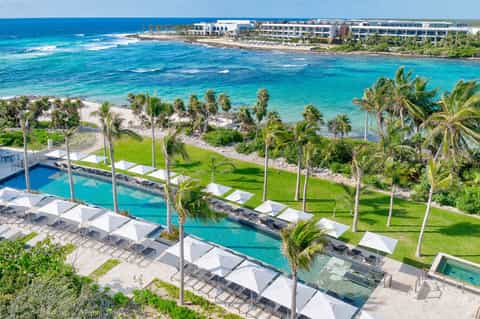 Aerial view of resort pool complex with multi-level pools, lawn, and turquoise ocean beyond