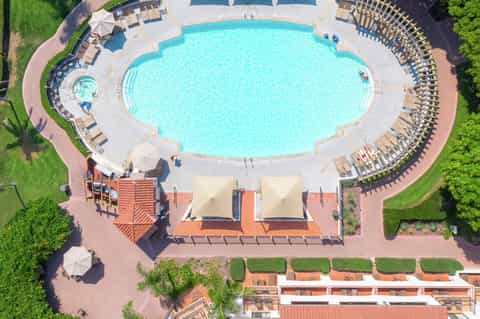 Aerial view of resort oval pool surrounded by lounge chairs and manicured grounds