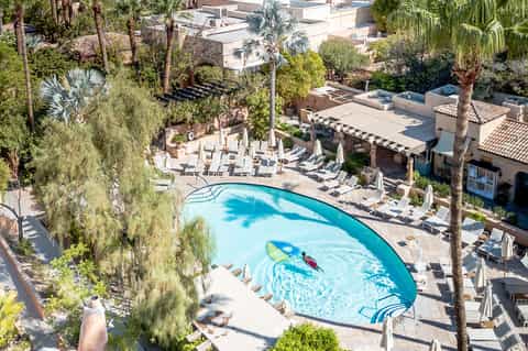 Aerial view of resort pool surrounded by lounge chairs, umbrellas, and palm trees