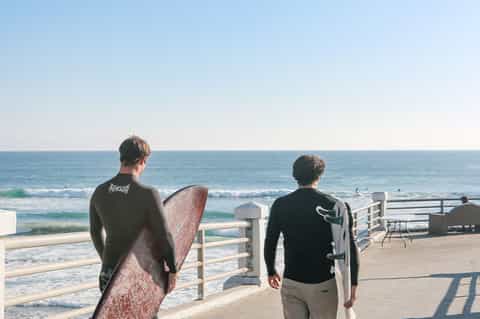 Surfers with boards standing on beachfront deck overlooking ocean waves