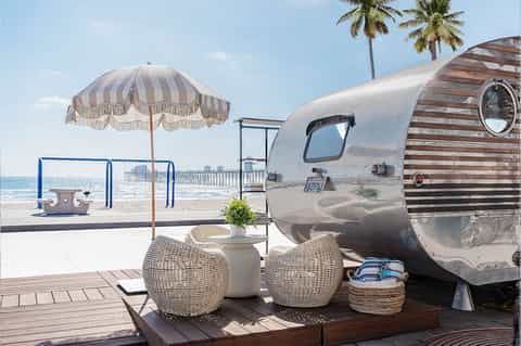 Vintage silver Airstream trailer on beach deck with umbrella, palm trees, and ocean view
