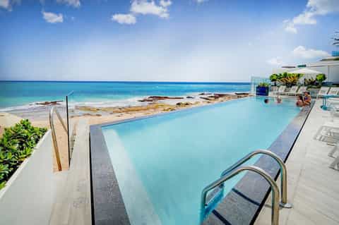 Modern infinity pool overlooking rocky coastline and turquoise ocean with lounge chairs