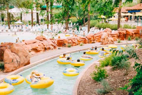 Lazy river with yellow inflatable tubes winding through a resort with red rock formations and beach area