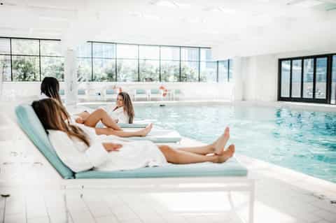 Modern indoor heated pool with lounge chairs, floor-to-ceiling windows, and spa-like ambiance