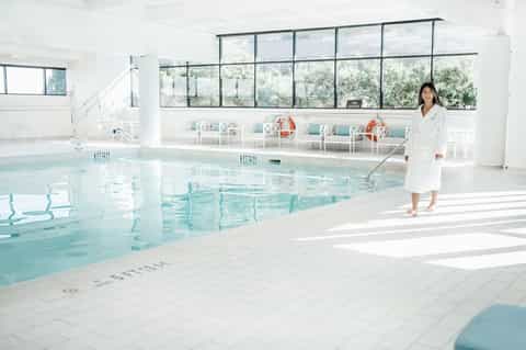 Bright indoor pool facility with floor-to-ceiling windows and seating areas