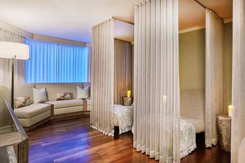 Luxurious spa suite with four-poster bed, flowing curtains, ambient lighting, and curved seating area