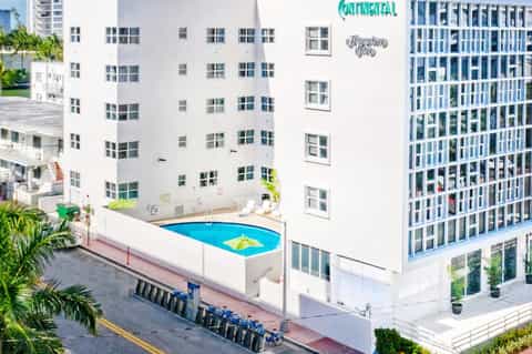 Aerial view of small blue hotel pool with yellow raft between white residential buildings