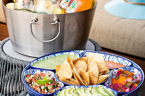 Appetizer platter with chips, salsa, guacamole, and tropical drinks in ice bucket