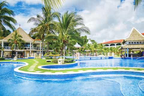 Expansive tropical resort with multiple pools, lush gardens, and thatched-roof structures