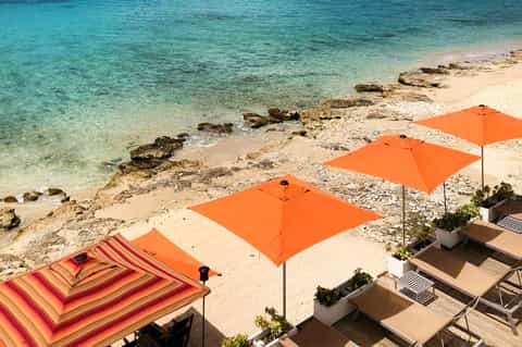 Beachfront view with three orange umbrellas on sand, crystal-clear turquoise water