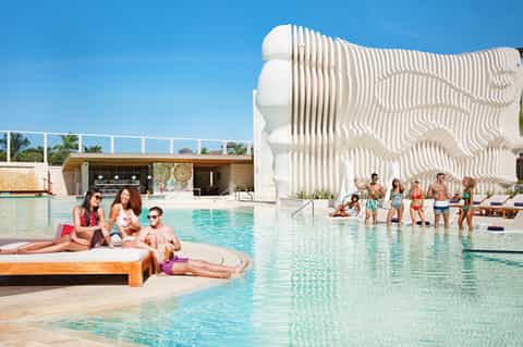 Modern resort pool with architectural white sculptural structure and guests enjoying the water