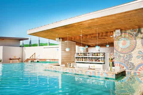 Indoor pool with turquoise water, wooden ceiling, geometric tile accents, modern bar, and architectural design