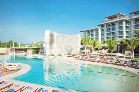 Modern resort pool with sculptural white architecture, orange lounge chairs, and high-rise hotel building