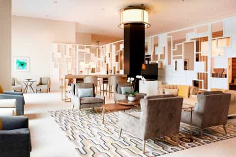 Spacious modern hotel lobby with geometric wall design, fireplace, seating areas, and skylights