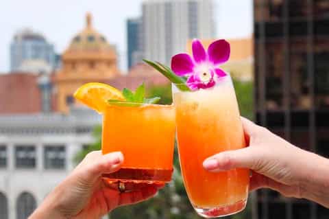 Two tropical cocktails with orange juice and pink orchid flowers, city skyline with golden dome in background