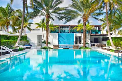 Luxurious resort pool with crystal-clear turquoise water, palm trees, and modern white architecture