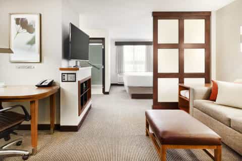 Modern hotel suite with living area, work desk, sofa, and bedroom visible through open doors