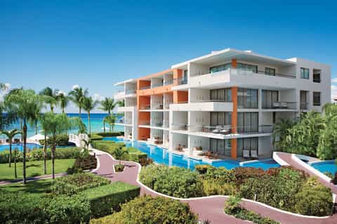 Modern beachfront resort building with white and orange architecture, multiple balconies, pools, and tropical landscaping