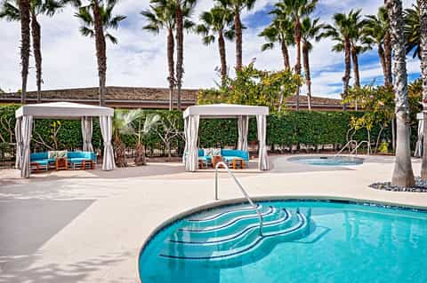 Resort pool deck with cabanas and palm trees under blue sky