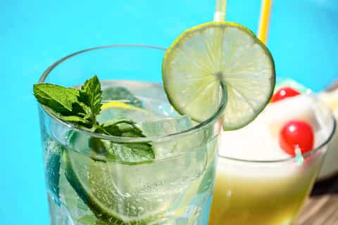 Tropical cocktail with lime slice and mint garnish on bright blue background