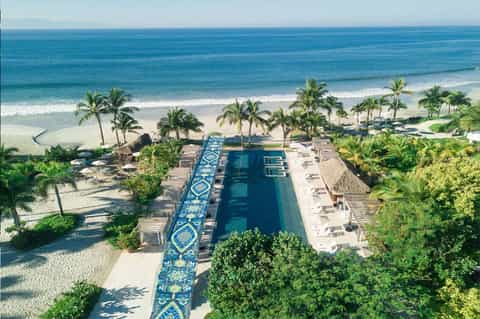 Aerial view of beachfront resort pool, ocean, white sand, palm trees, and coastal landscape