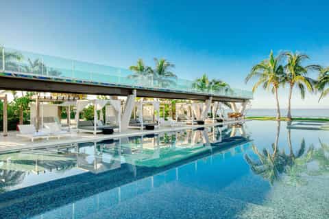 Infinity pool with white pergolas and palm trees reflecting in calm turquoise water