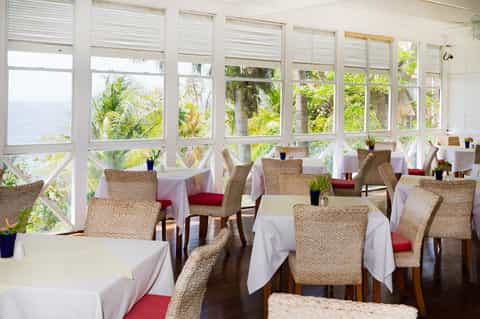 Waterfront dining room with wicker chairs, white tablecloths, and water views