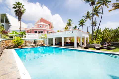 Pink and white residential property with pool, stone accents, and palm trees