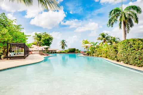 Resort lap pool surrounded by palm trees, lounge chairs, daybed with canopy, and tropical landscaping