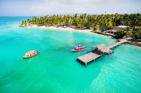 Aerial view of tropical island with turquoise lagoon, boats, dock, and palm tree shoreline