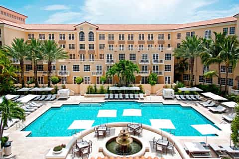 Luxury resort courtyard with large pool, fountain, palm trees, and cream-colored building