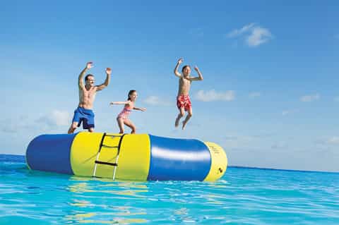 Four children jumping on yellow and blue inflatable water trampoline in ocean
