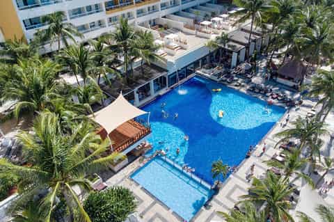 Aerial view of resort pool complex with palm trees, lounge chairs, and hotel building