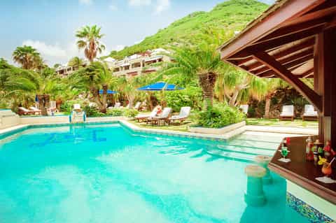 Lagoon-style resort pool nestled in lush tropical setting with mountain backdrop and lounge areas