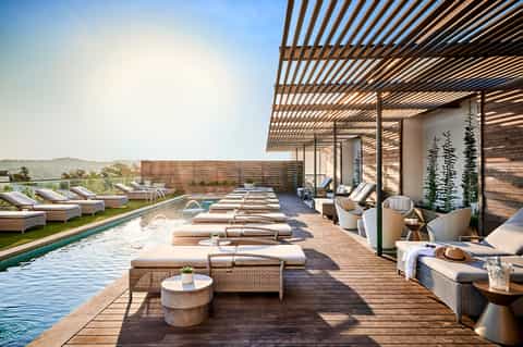 Luxury rooftop pool terrace with lounge chairs, wood decking, and scenic hillside views at dusk