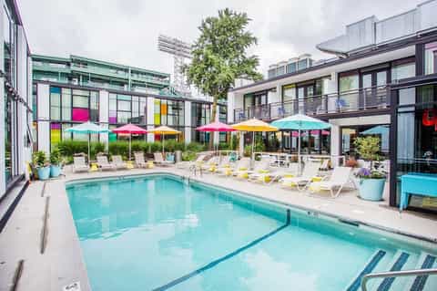 Contemporary pool area with colorful umbrellas, modern buildings, and lounge chairs