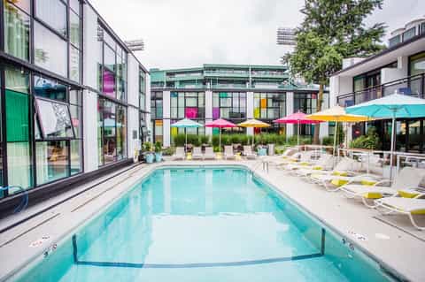 Modern outdoor pool with colorful umbrellas, lounge chairs, and contemporary hotel building with large windows