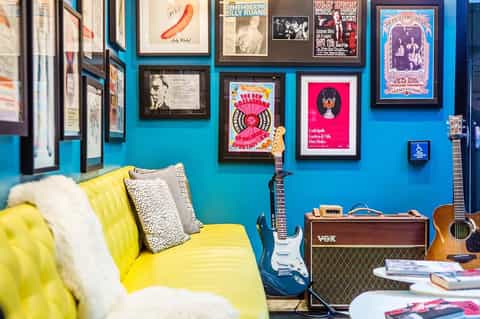 Music-themed room with yellow sofa, guitars, amplifier, and framed concert posters on turquoise wall