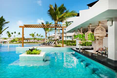Luxury resort pool with swim-up bar, wooden pergola, and palm trees