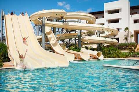 Water park with multiple tall cream-colored slide towers and children splashing in pool