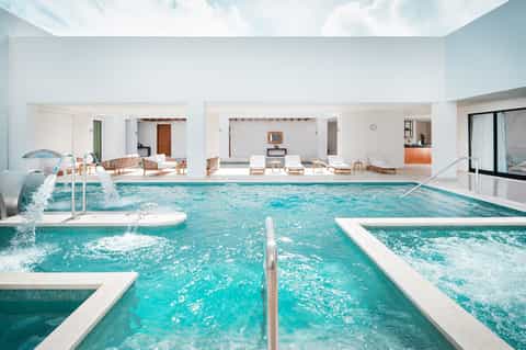 Indoor pool facility with turquoise water, white lounges, and skylit ceiling in spa-like setting