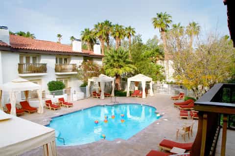 Resort pool with colorful umbrellas, white cabanas, palm trees, and Spanish colonial architecture