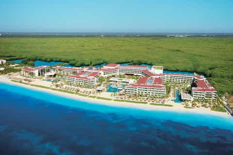 Aerial view of beachfront all-inclusive resort with red roofs, pools, and pristine white sand