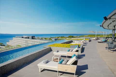 Infinity pool along oceanfront terrace with modern loungers, umbrellas, and coastal landscape
